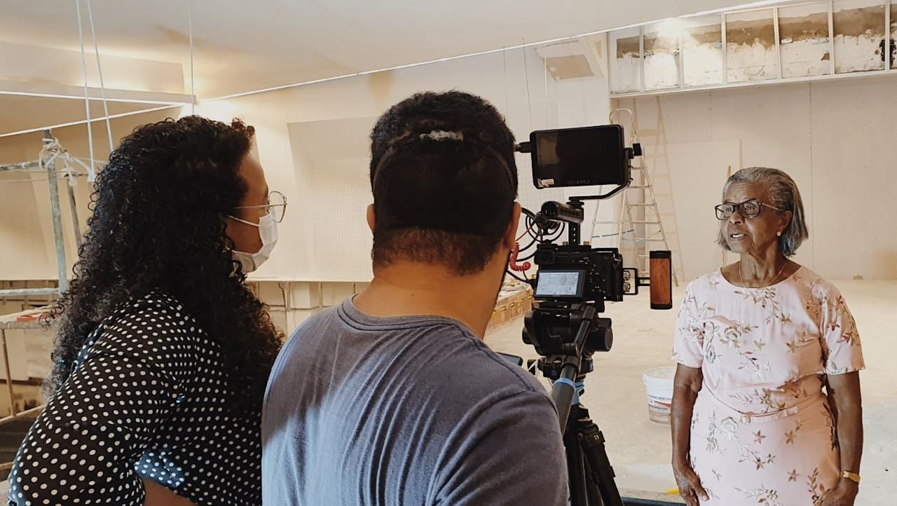 Letícia em entrevista de captação de vídeo, com câmera e monitor